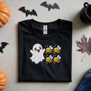 May include: A black short-sleeved t-shirt featuring a graphic print of a white cartoon ghost with a happy expression positioned next to four small yellow and black striped bees with light blue wings, arranged in a square formation on the chest.