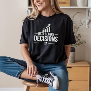 Peut inclure: Un t-shirt noir à manches courtes avec une impression graphique blanche sur la poitrine. Le motif comprend un graphique à barres orienté vers le haut, le texte "DATA BEFORE DECISIONS" en police sans empattement et une petite icône de graphique.