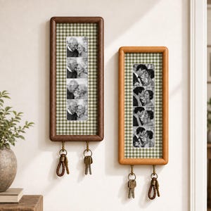 May include: Two rectangular wall-mounted wooden frames with dark and light wood finishes. Each frame features a green and white gingham background and a vertical strip of four black and white photographs. Two metal hooks at the bottom hold keys.