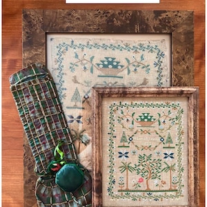 May include: Two framed cross-stitch samplers with floral and tree designs, and a plaid fabric item. The samplers are in wooden frames. The text "Hannah Leuty 1825" is visible. The text "Chart and history by Collector With A Needle" is also visible.