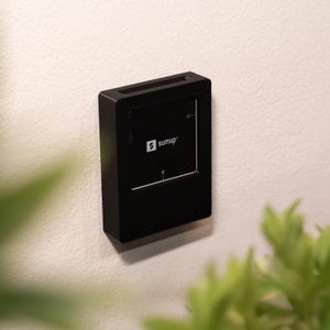 Könnte beinhalten: Ein schwarzes, rechteckiges Kartenlesegerät, das an einer Wand montiert ist. Das Gerät verfügt über ein schwarzes Bedienfeld mit dem weißen SumUp-Logo, einem Power-Symbol und einem USB-Symbol. Es steckt in einem schwarzen Rahmen mit Schlitz.
