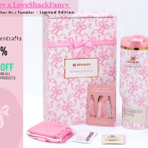 May include: A 40oz Stanley x LoveShackFancy Quencher H2.0 tumbler with a pink ribbon pattern, a matching gift box, a pink drawstring pouch, a small informational card, and a long pink straw with a bow topper, all featuring the Stanley brand logo.