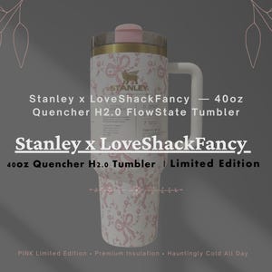 May include: A 40oz Stanley x LoveShackFancy Quencher H2.0 FlowState tumbler featuring a white body with a pink ribbon and floral pattern. The tumbler has a gold-tone rim, a pink lid, and a white handle. Text includes Stanley x LoveShackFancy.
