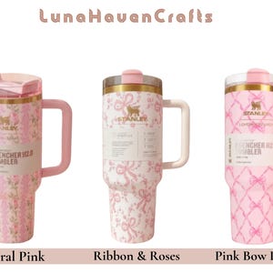 May include: Three Stanley Quencher H2.0 tumblers with handles and lids. The first features a pink floral pattern, the second a pink ribbon and rose design, and the third a pink bow lattice pattern. Each tumbler displays the Stanley logo and branding.