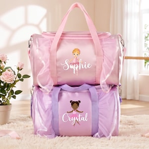 Könnte beinhalten: Zwei zylindrische Sporttaschen mit gerüschtem Tüllbesatz. Die obere Tasche ist rosa mit dem Namen Sophie und einer Ballerina-Grafik. Die untere Tasche ist lavendelfarben mit dem Namen Crystal und einer Ballerina-Grafik, beide mit Tragegriffen.
