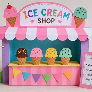 Könnte beinhalten: Ein Eisdielen-Spielset aus Papier mit einer rosa-weiß gestreiften Markise, einem Schild mit der Aufschrift ICE CREAM SHOP und vier Eistüten in Schokolade, Erdbeere, Vanille und Minze. Enthält ein OPEN-Schild und eine Menütafel.