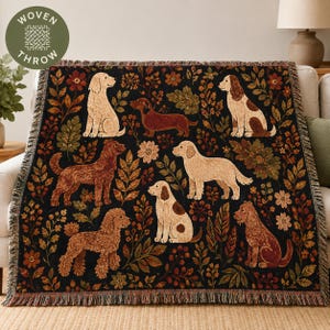 May include: A woven throw blanket featuring a black background with a repeating pattern of various dog breeds, including golden retrievers, a dachshund, and a poodle, interspersed with colourful autumn leaves and small floral elements.