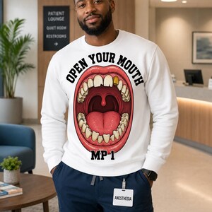 May include: A white long-sleeve sweatshirt featuring a graphic of an open mouth with visible teeth, including one gold tooth, and the text "OPEN YOUR MOUTH" arched above and "MP-1" printed below the graphic in bold black lettering.