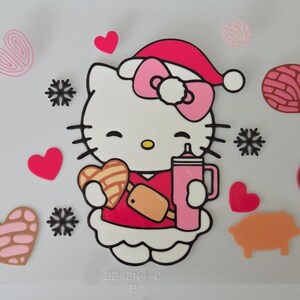 Puede incluir: Una calcomanía con un gato de dibujos animados blanco con un lazo rosa y un gorro de Papá Noel rojo, sosteniendo una galleta en forma de corazón y un vaso rosa. El diseño incluye iconos como corazones rosas, siluetas de animales y copos de nieve.