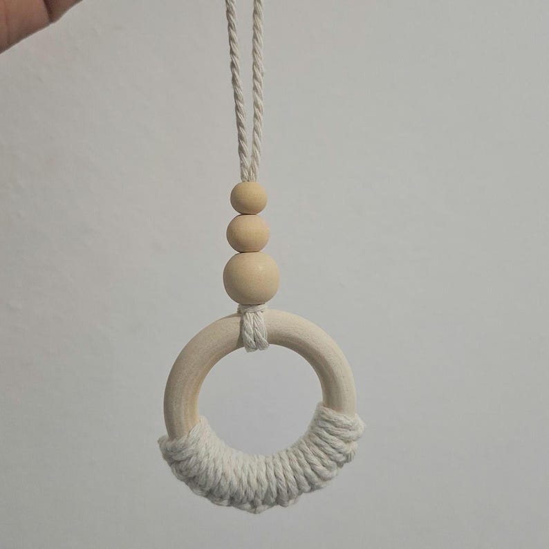 May include: A hanging ornament featuring a smooth wooden ring partially wrapped in off-white cotton cord. Above the ring are three graduated wooden beads strung on a matching cotton cord, which extends upward to form a loop for hanging purposes.