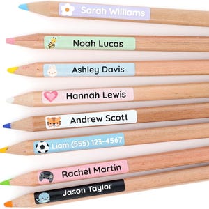 Op de afbeelding: Acht houten potloden met gekleurde punten en gepersonaliseerde zelfklevende labels. Elk label bevat een uniek icoon en een naam, waaronder Sarah Williams, Noah Lucas, Ashley Davis, Hannah Lewis, Andrew Scott, Liam (555) 123-4567, Rachel Martin en Jason Taylor.