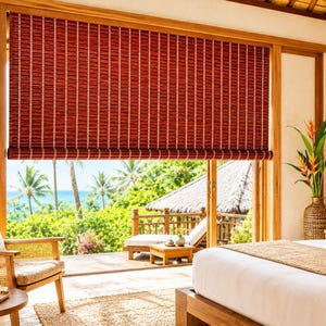 May include: A roll-up window shade made of thin, dark red bamboo slats held together by vertical white strings. The shade is mounted inside a wooden frame, covering the upper portion of a large glass door that overlooks a tropical landscape.