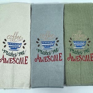 May include: Three waffle-weave kitchen towels in cream, gray, and green. Each towel features an embroidered coffee cup design with the words "coffee makes me AWESOME" in a whimsical font. The towels are folded.