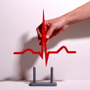 Könnte beinhalten: Eine leuchtend rote, flache, zweidimensionale Darstellung eines menschlichen Herzrhythmus, speziell eine Elektrokardiogramm- oder EKG-Linie mit einer scharfen, vertikalen Spitze. Die rote Herzrhythmusform befindet sich über einem grauen Sockel.