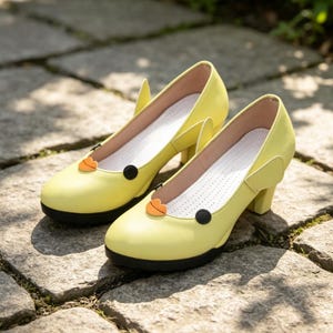 Peut inclure: Une paire d'escarpins jaune vif avec un bout arrondi, un talon bloc et une semelle intérieure blanche perforée. Chaque chaussure est ornée d'un petit accent orange en forme de lèvres et d'un détail circulaire noir sur le dessus, avec des ailettes.