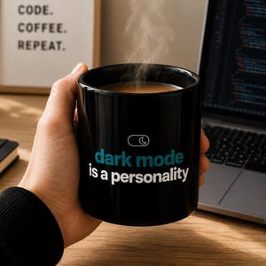 May include: A black ceramic mug filled with a steaming hot beverage. The mug features a white and teal graphic of a toggle switch icon above the text "dark mode is a personality" printed in a clean, sans-serif font on the front surface.