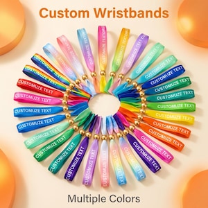 May include: A collection of fabric wristbands arranged in a circular pattern, featuring various solid colours and rainbow gradients. Each wristband includes a gold-toned metal bead and the white printed text CUSTOMUZE TEXT. The image includes the text Custom Wristbands and Multiple Colours.