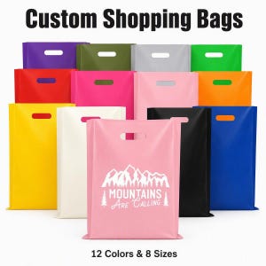 Puede incluir: Una colección de bolsas de compra rectangulares de plástico con asas troqueladas, disponibles en doce colores sólidos incluyendo rojo, amarillo, rosa, negro y azul. Una bolsa rosa claro presenta un gráfico blanco de montañas y el texto Mountains Are Calling.
