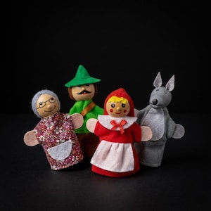 Könnte beinhalten: Ein Set aus vier Fingerpuppen, bestehend aus einer Großmutter im Blumenkleid, einem Jäger mit grünem Hut, einem Kind mit roter Kapuze und weißer Schürze sowie einem grauen Wolf. Jede Puppe hat einen bemalten Holzkopf mit Gesichtszügen.