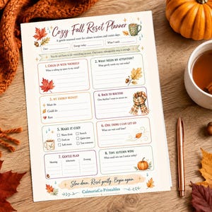 Könnte beinhalten: Eine gedruckte Planerseite mit dem Titel Cozy Fall Reset Planner, die Abschnitte für tägliche Check-ins, Energiebudgets und herbstliche Ziele enthält. Das Dokument zeigt Illustrationen von Ahornblättern, einem Schal, einem Kürbis und einer Tasse.