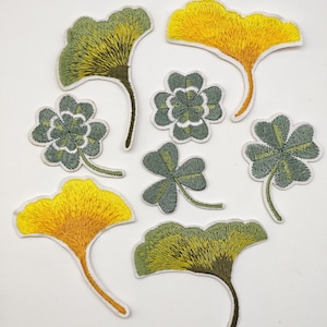 Peut inclure: Un ensemble d'écussons en tissu brodé représentant des motifs botaniques. Le lot comprend trois formes de feuilles de ginkgo aux dégradés jaune et vert, trois trèfles à quatre feuilles dans des tons verts et un trèfle à trois feuilles vert.