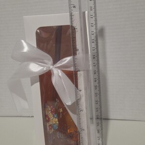 May include: A rectangular white gift box with a clear window containing a glass item with a floral graphic and the text "Enjoy the little things". A white satin ribbon is tied around the box. A clear plastic ruler shows the box is 6 inches tall.
