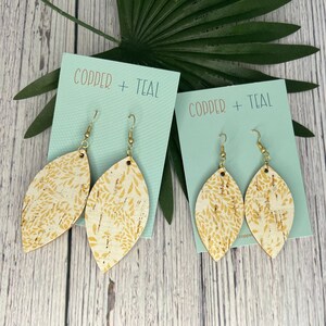 May include: Two pairs of cork earrings with a gold leaf pattern. The earrings are on teal cards with the text "Copper + Teal".
