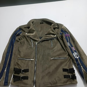 May include: An olive green corduroy motorcycle jacket featuring a diagonal front zipper, silver-tone hardware, and two zippered chest pockets. The sleeves have dark blue vertical stripes, zippers at the cuffs, and several embroidered patches.
