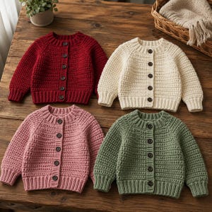 Könnte beinhalten: Vier langärmelige Strickjacken mit Knopfleiste in den Unifarben Dunkelrot, Creme, Hellrosa und Salbeigrün. Jeder Pullover hat eine gerippte Strickstruktur, einen Rundhalsausschnitt und eine vertikale Reihe dunkelbrauner Knöpfe vorne.