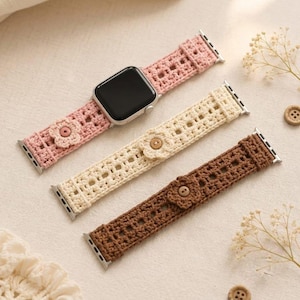 May include: Three crochet watch bands in pink, cream, and brown, each featuring a small flower accent with a central button. The pink band is attached to a black smartwatch, while the cream and brown bands are shown as separate accessories.