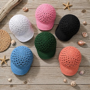 Può includere: Una collezione di sei cappellini da baseball realizzati in filato lavorato all'uncinetto nei colori bianco, rosa, nero, verde scuro, blu e corallo. Ogni cappellino presenta una visiera strutturata e un motivo a trama aperta sulla calotta.