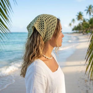 May include: A sage green crochet bandana head covering featuring an openwork diamond pattern. The triangular headscarf is crafted from yarn and is tied at the back of the head, providing a textured, lightweight accessory for covering the hair.