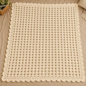 Può includere: Una coperta rettangolare all'uncinetto color crema caratterizzata da un motivo a griglia ripetuto con piccole aperture quadrate. I bordi della coperta sono rifiniti con un bordo decorativo smerlato composto da punti arrotondati.