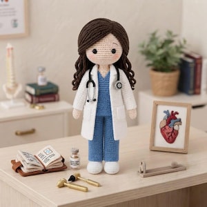 Puede incluir: Una muñeca de ganchillo vestida de profesional médico, con cabello largo castaño, bata blanca y uniforme azul. La muñeca lleva un estetoscopio negro alrededor del cuello. Los accesorios incluyen un pequeño libro abierto, un frasco y dos herramientas doradas.