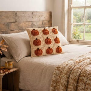 Peut inclure: Un coussin carré au crochet composé d'une grille de neuf carrés individuels, chacun présentant un motif de citrouille orange texturé et en relief sur un fond crème. Le coussin est réalisé avec des points de laine visibles et un design plat.