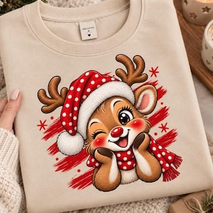 Op de afbeelding: Een beige sweater met ronde hals voorzien van een afbeelding van een cartoonrendier met grote ogen, een rode neus en een rood-witte muts en sjaal met stippen. Het rendier knipoogt en rust met de kin op de handen tegen een rode achtergrond.