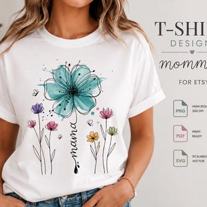 Op de afbeelding: Een wit t-shirt met een aquarel-stijl afbeelding van een grote blauwgroene bloem en diverse kleinere kleurrijke wilde bloemen in roze, paars, geel en groen. Het woord mama staat in cursief schrift langs de steel van de centrale bloem.