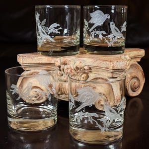 May include: A set of four clear glass tumblers, each featuring a frosted white etched design of birds perched on branches. The glass on the top left includes the signature jjames etched in white near the base of the glass vessel.