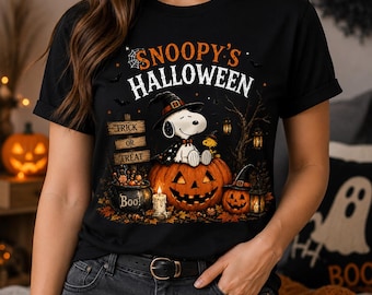 May include: A black t-shirt featuring a graphic of Snoopy wearing a witch hat, sitting on a large jack-o'-lantern. The design includes the text "SNOOPY'S HALLOWEEN", a "TRICK OR TREAT" sign, a cauldron labeled "BOO!", a candle, and a smaller pumpkin.
