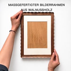 May include: A rectangular picture frame crafted from dark brown walnut wood with a scalloped edge design. The frame features a cream-colored mat board surrounding a central light brown wood panel. The text MASSGEFERTIGTER BILDERRAHMEN AUS WALNUSSHOLZ is visible.