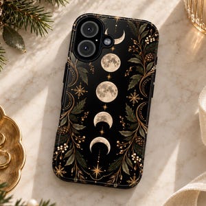May include: A black smartphone case featuring a vertical sequence of moon phases from crescent to full moon. The design is accented with gold-toned botanical illustrations, including leaves, pine cones, and small starbursts, arranged along the sides.