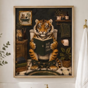 May include: A framed wall art print depicting a tiger sitting on a toilet reading a green book titled EAT, PRAY, LOVE. The tiger is orange with black stripes, set in a bathroom scene with a wooden cabinet, a small potted plant, and a towel.