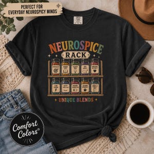 Peut inclure: Un t-shirt noir à manches courtes avec un motif de deux étagères en bois contenant dix bocaux en verre. Le texte indique NEUROSPICE RACK et UNIQUE BLENDS. Chaque bocal contient des éléments colorés et des étiquettes comme HYPERFOCUS et STIM SEEKING.