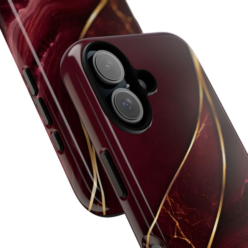May include: A smartphone case featuring a deep burgundy and dark red marble pattern with flowing gold veins. The case has a dual-camera cutout with a black border, black side buttons, and a smooth, glossy finish that covers the back and sides.