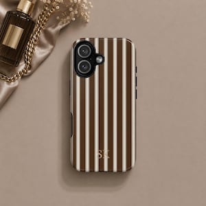 K&ouml;nnte beinhalten: Eine Smartphone-H&uuml;lle mit vertikalem Streifenmuster in Dunkelbraun und Creme. Die H&uuml;lle hat oben links einen Ausschnitt f&uuml;r eine Doppelkamera und die goldfarbenen Initialen SK in einer Serifenschrift unten in der Mitte der R&uuml;ckseite.