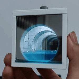 May include: A square white frame containing an infinity mirror effect that displays a repeating tunnel with white tiled walls and a pool of blue liquid at the base. The device features a metallic knob on the top edge and a reflective glass front.