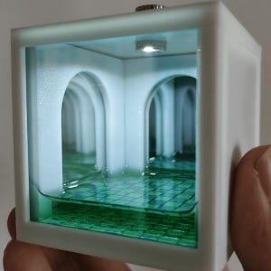 May include: A white cube-shaped display box featuring an internal miniature room with arched doorways and a green checkered floor. The interior is illuminated by a small overhead light, creating a reflective effect that mimics a deep hallway.