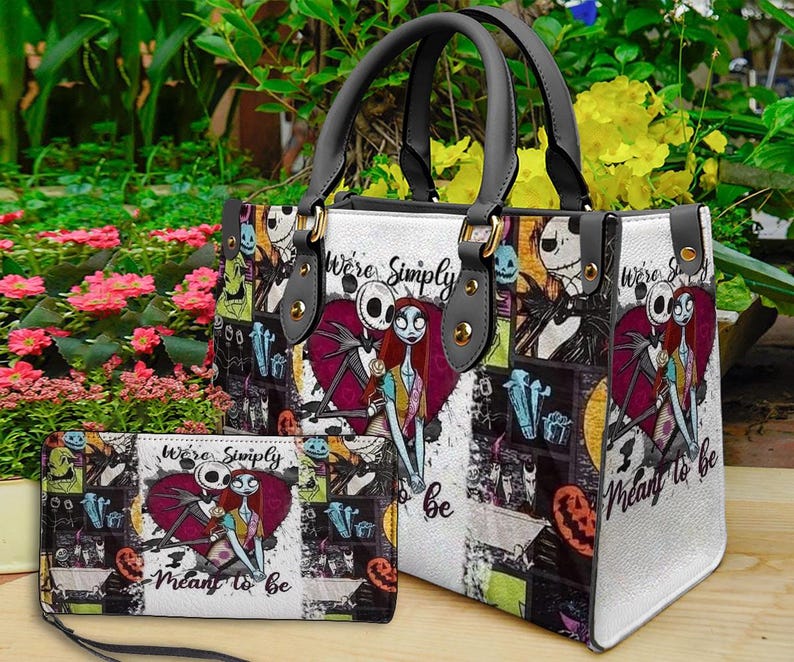 May include: A structured handbag and matching rectangular wallet featuring a collage print of Jack Skellington and Sally from The Nightmare Before Christmas, with the text "We're Simply Meant to Be" and dark grey handles with gold-tone hardware.