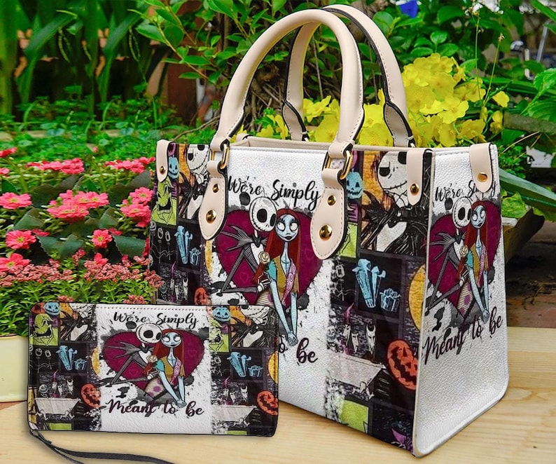 May include: A white handbag and matching rectangular wallet featuring a collage print of Jack Skellington and Sally from The Nightmare Before Christmas. The design includes the text "We're Simply Meant to Be" and various character graphics.