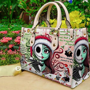 May include: A structured handbag featuring a split-face character design of a skeleton and a stitched doll wearing a Santa hat. The bag includes cream-colored handles, gold-tone hardware, and a repeating pattern of holiday-themed text and graphics.